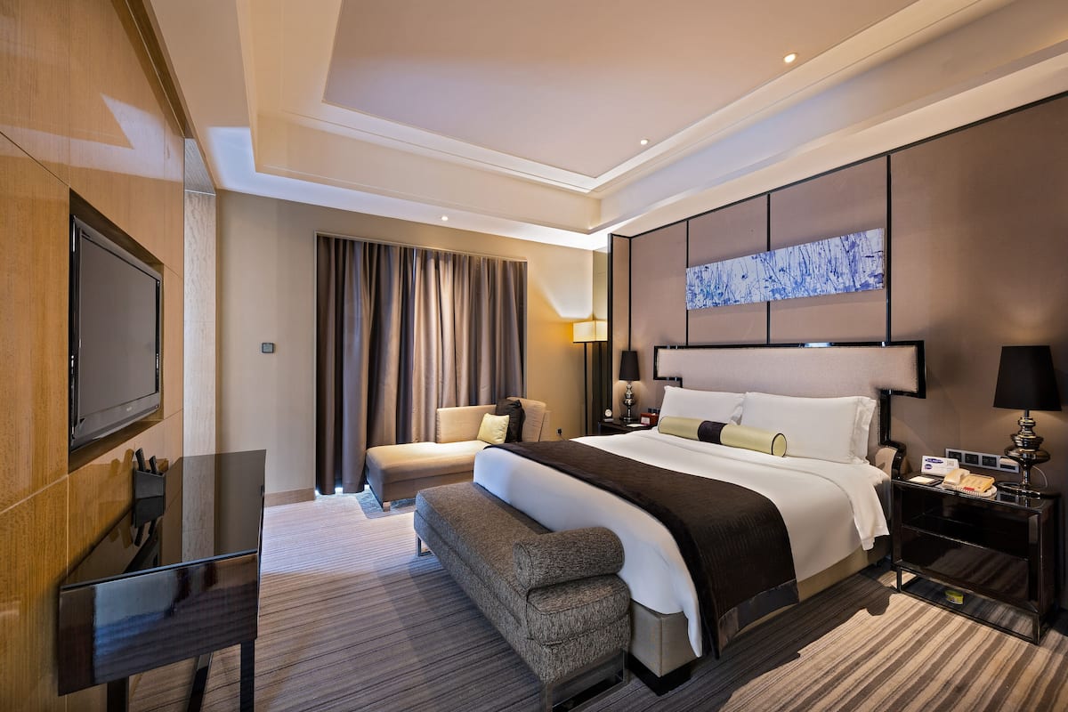 Une chambre d’hôtel moderne équipée d’un grand lit, d’un canapé, d’une télévision et d’un bureau avec une lampe.