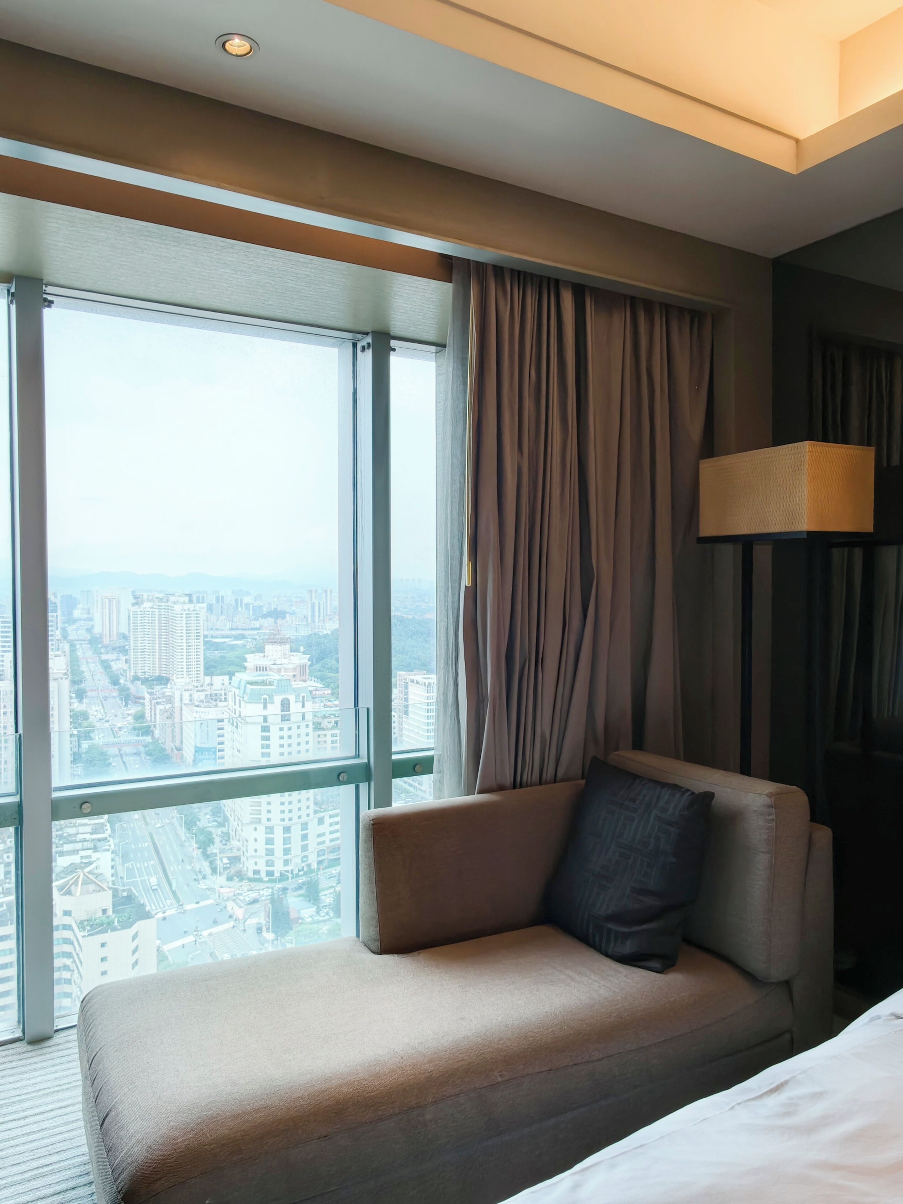 A hotel room with a large window, a sofa, a lamp, and a bed.