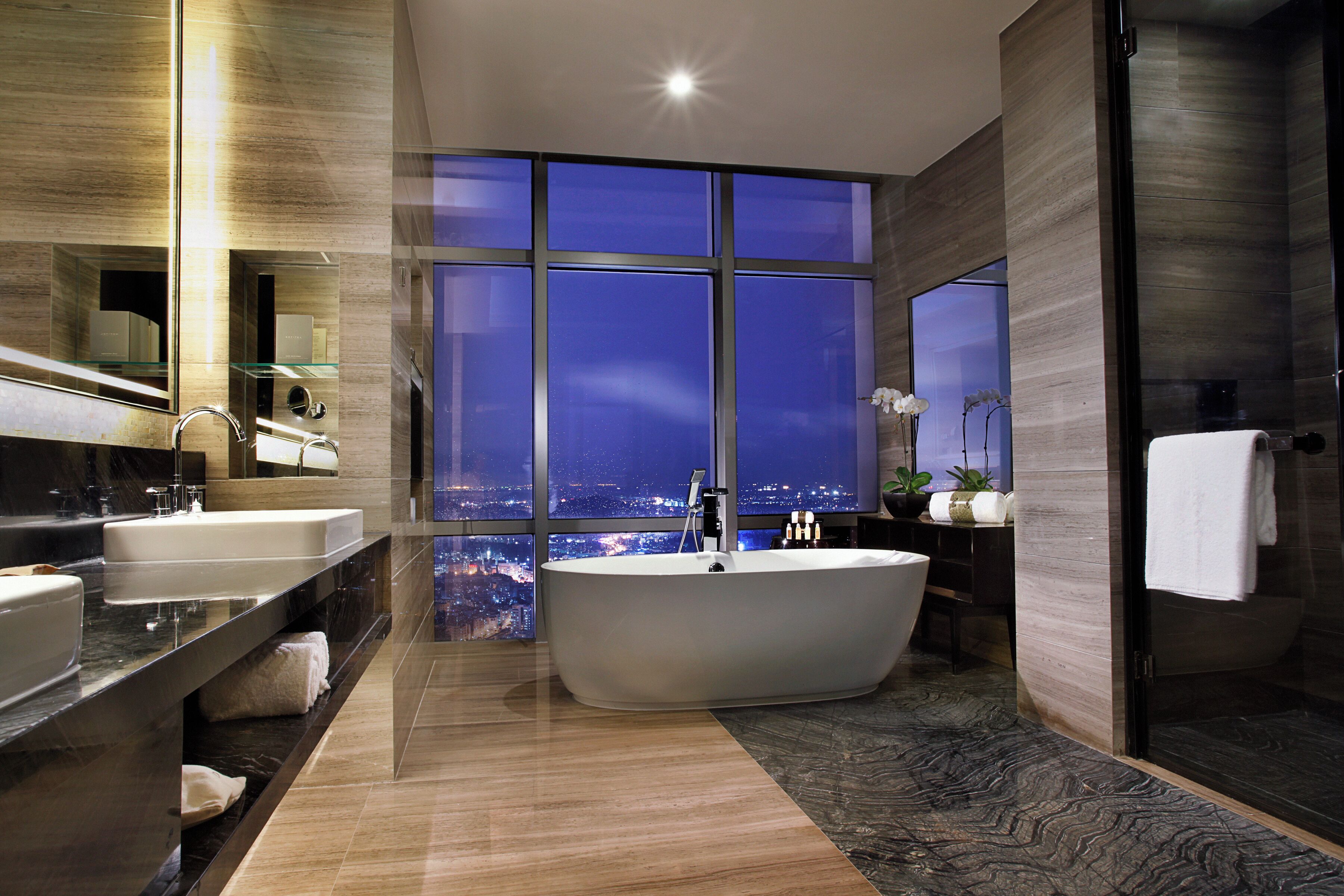 A modern bathroom with a freestanding bathtub, dual sinks, and a large window offering a city view.