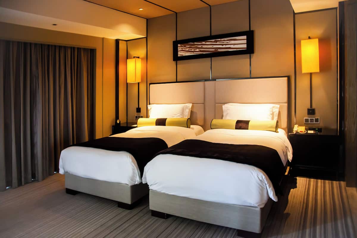 A hotel room with two beds, a large window with curtains, and two bedside lamps.