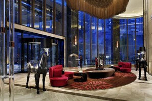 A modern lobby with a large glass wall, a red sofa, a black horse statue, and a circular rug. - Mels Weldon Dongguan Humen (Dongguan)