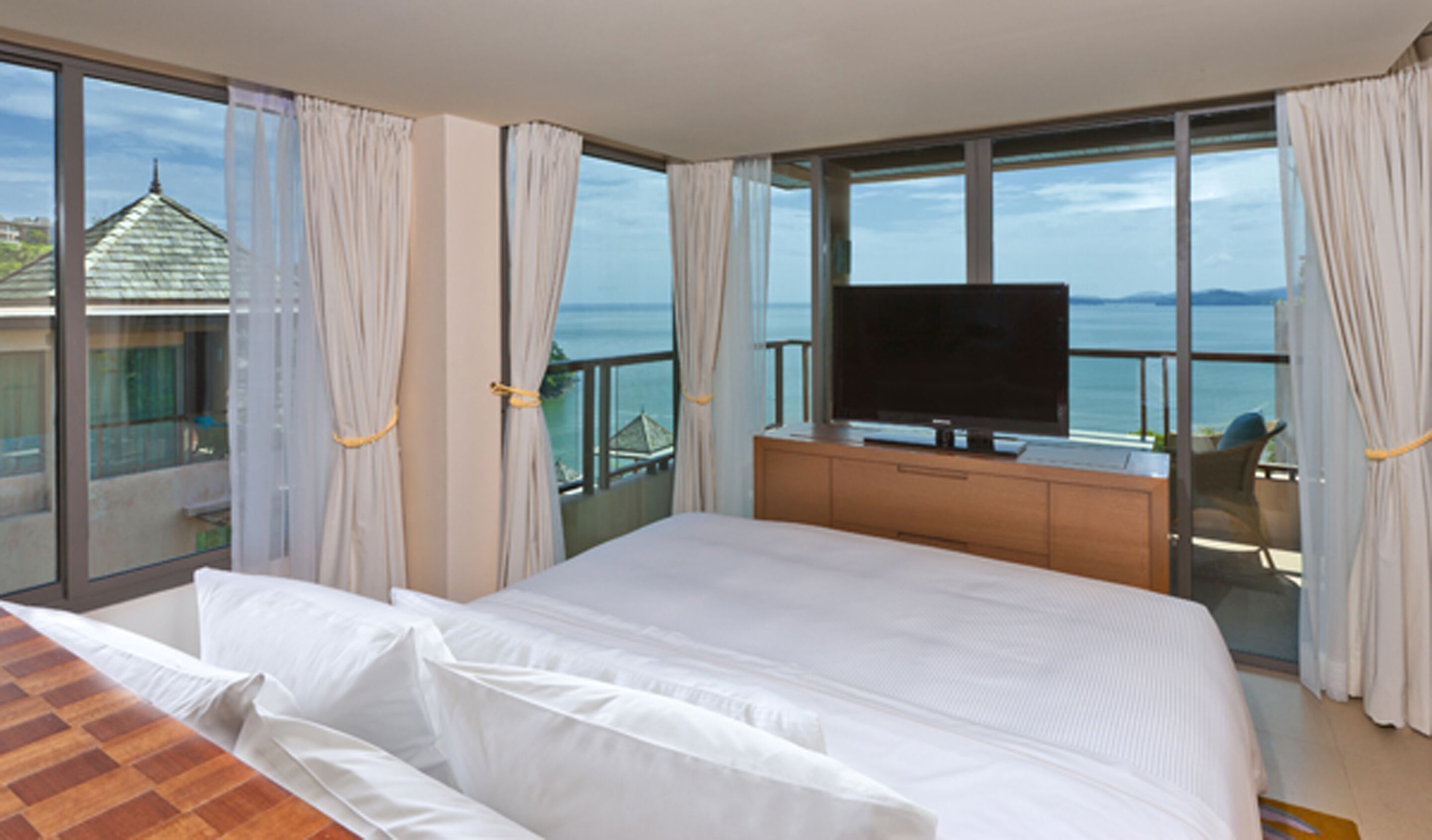 A bedroom with a large bed, a TV, and a balcony with a view of the sea.