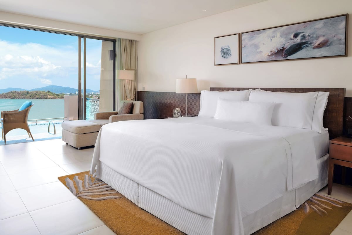 Une chambre d’hôtel avec un grand lit, une chaise, une table de chevet et une vue sur la mer.