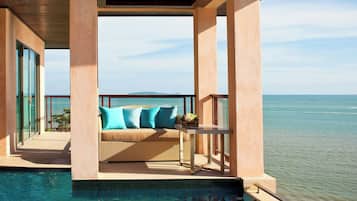 Una piscina infinita con cubierta de madera y zona de estar con cojines.