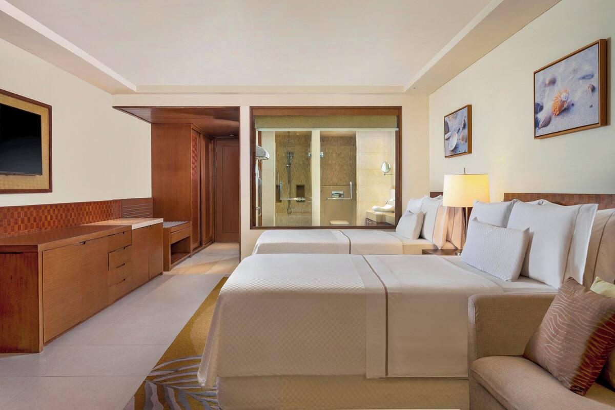 Une chambre d’hôtel avec un grand lit, un canapé, un bureau et une salle de bain visible à travers une porte en verre.