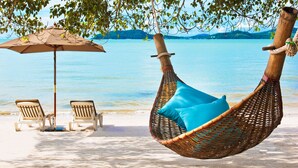 A beach setting with a hanging chair and two lounge chairs under an umbrella.