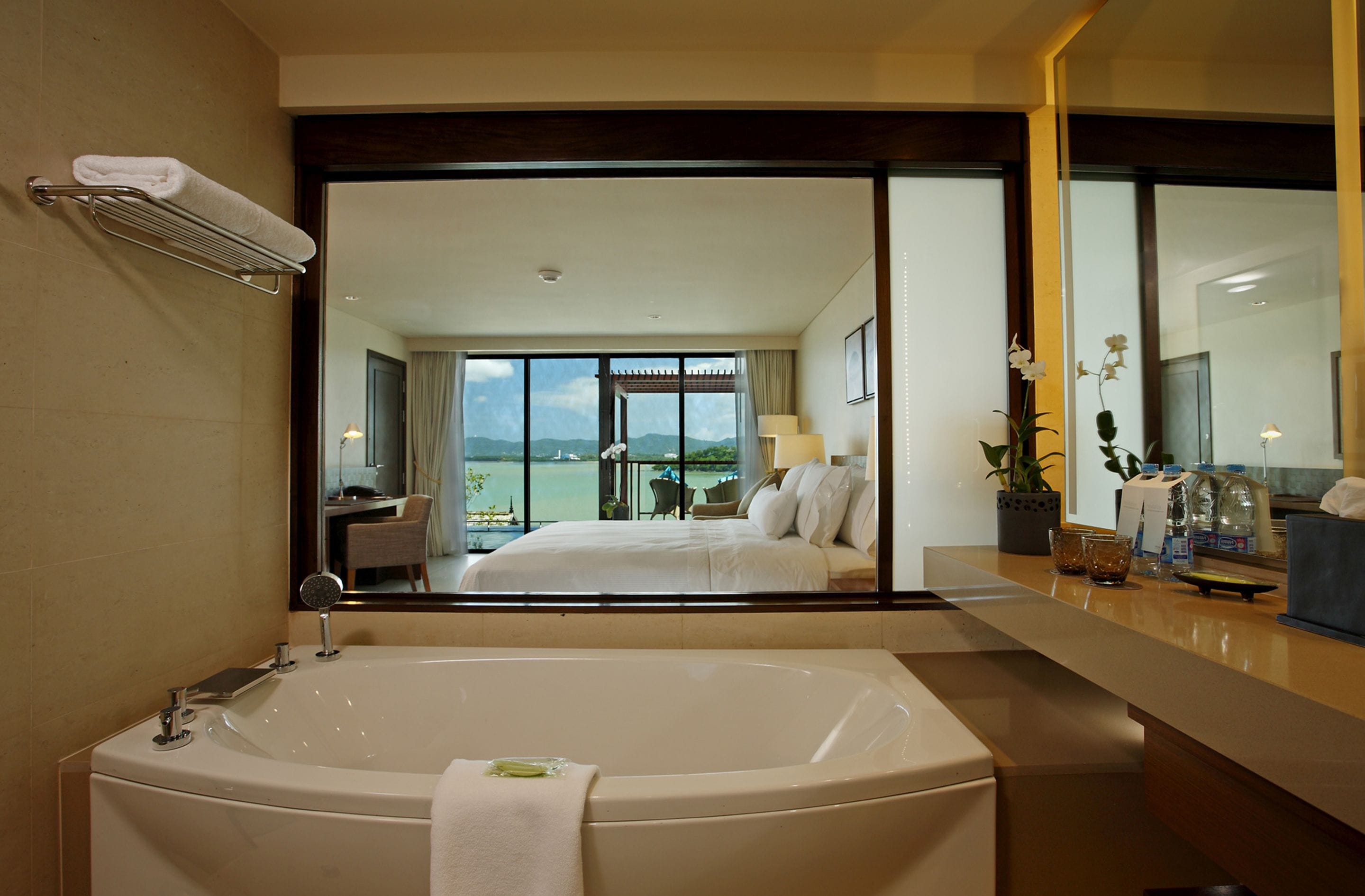 Ein modernes Hotelzimmer mit einer großen Badewanne, einem Balkon mit Meerblick und einem geräumigen Schlafzimmer mit einem großen Bett und einem Schreibtisch.