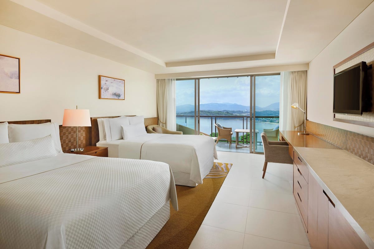 Une chambre d’hôtel avec deux lits, une télévision, un balcon donnant sur la mer et un coin repas.