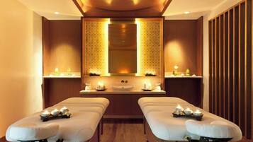 Experience rejuvenation in this serene spa room with two massage tables, a large mirror, and a warm atmosphere.