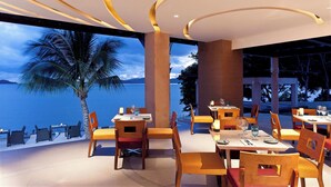 Ein Restaurant mit Tischen, Stühlen, einer Palme und Blick auf das Wasser.