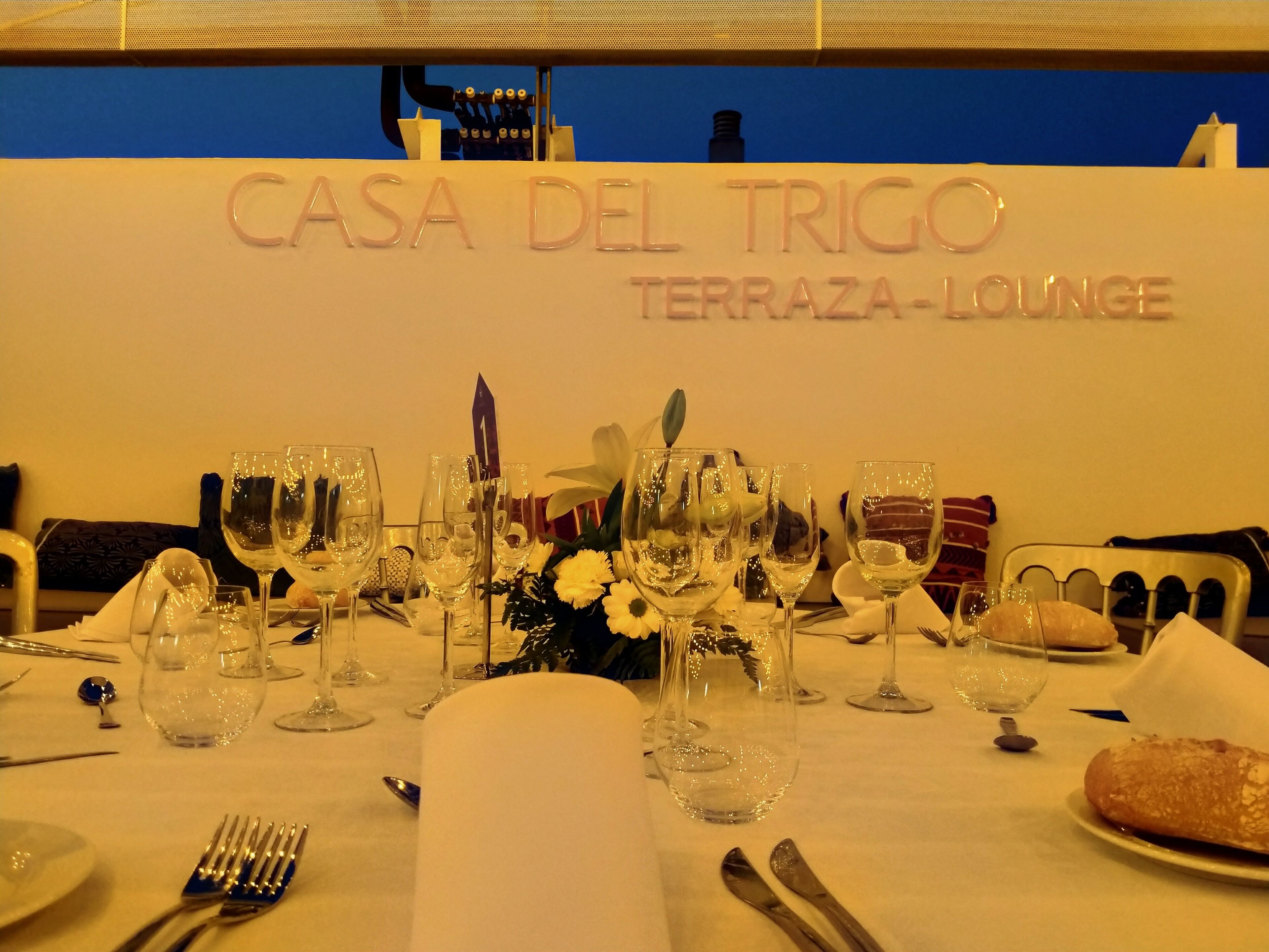 A well-set dining table at CASA DEL TRIGO TERRAZA-LOUNGE with multiple wine glasses, cutlery, and a loaf of bread.