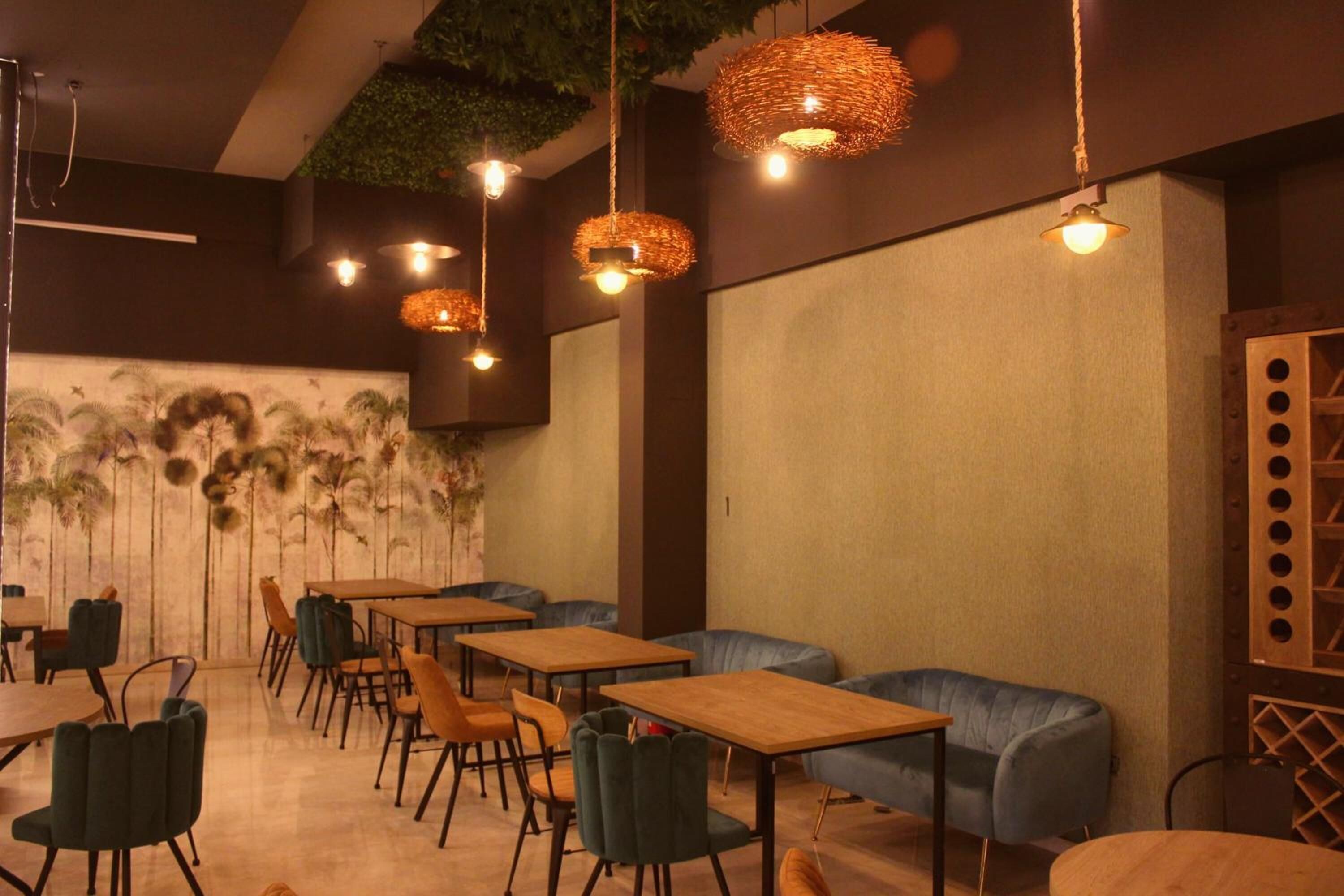 A restaurant with wooden tables and chairs, hanging wicker lamps, and a mural of palm trees on the wall.