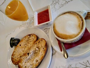 A breakfast setting with a plate of toasted bread, a cup of coffee with foam, a glass of orange juice, and a small dish of jam. - Casa Del Trigo (Santa Fe)