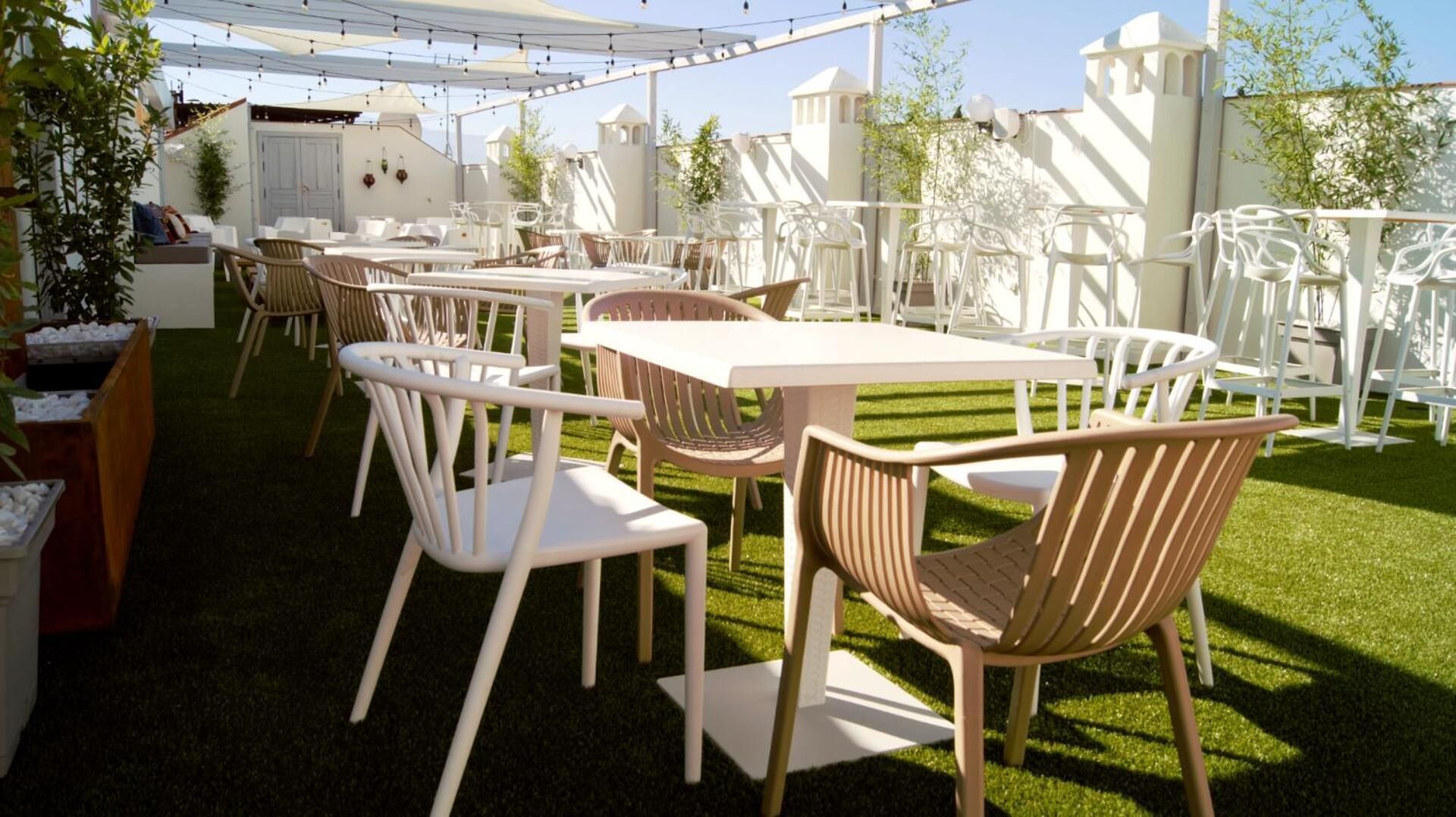 An outdoor seating area with white tables and chairs, surrounded by a white fence and greenery.