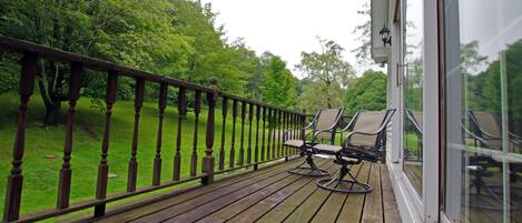 Een houten terras met twee stoelen, een leuning en een glazen deur die uitkomt op een tuin.