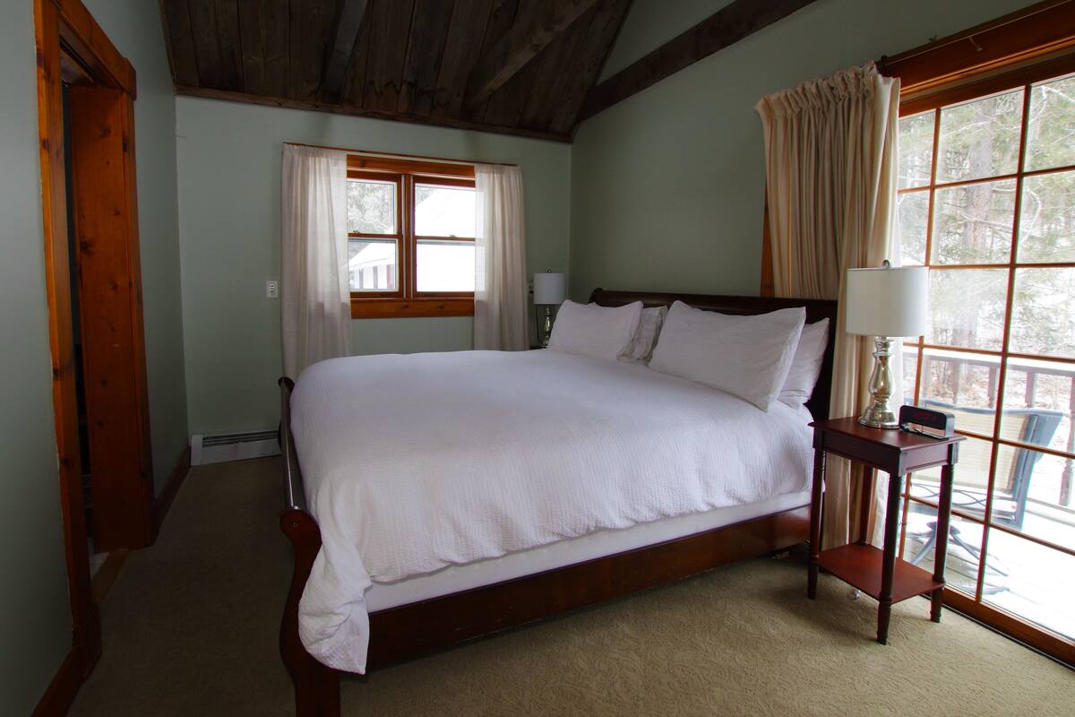 Un grand lit avec du linge de lit blanc, une tête de lit en bois et une table de chevet avec une lampe et une horloge.