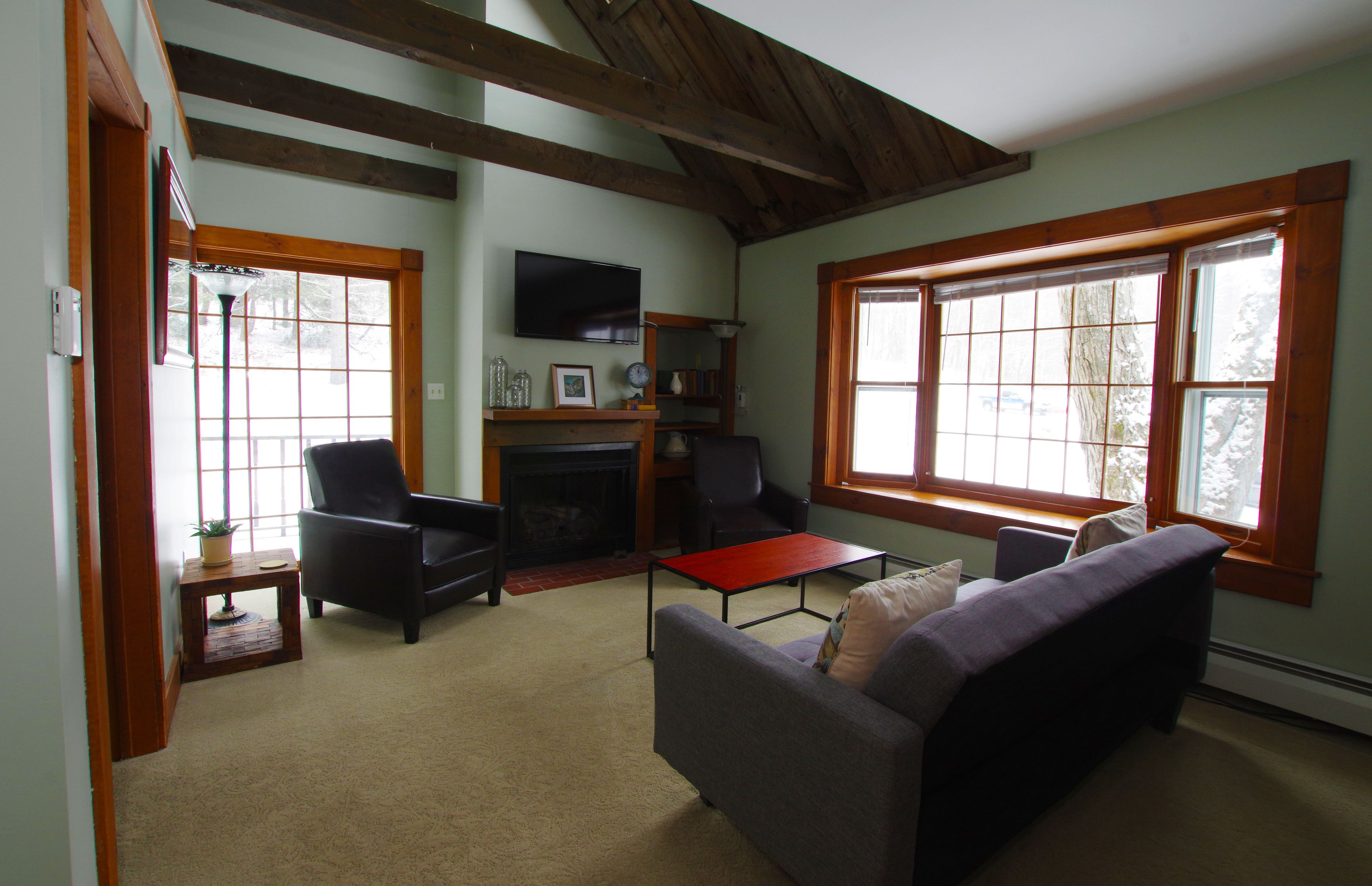 A cozy living room with a fireplace, comfortable seating, and large windows.