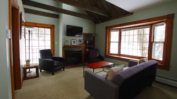 A cozy living room with a fireplace, comfortable seating, and large windows.