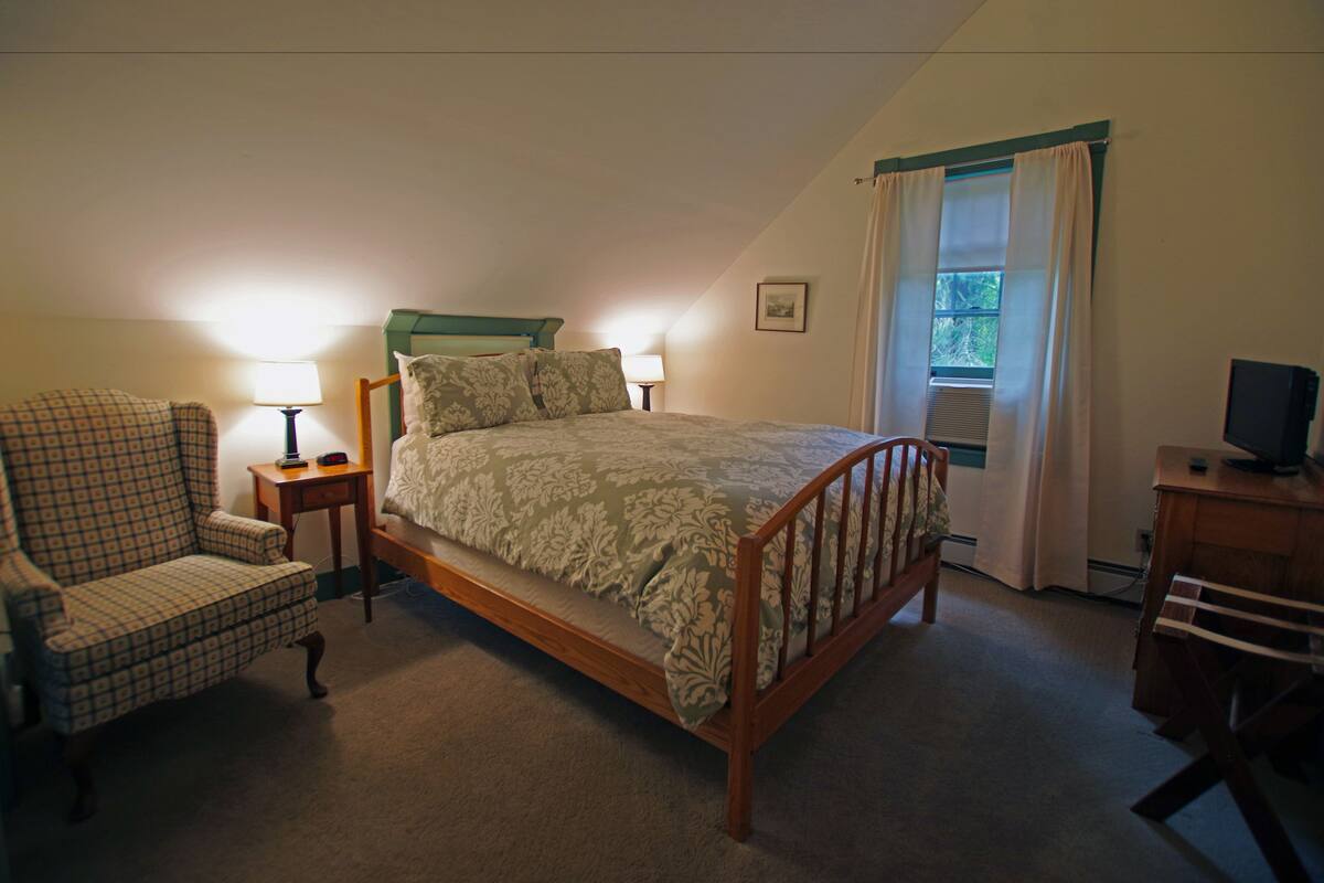 Une chambre avec un lit simple, une chaise, un bureau avec une télévision et une fenêtre avec des rideaux.