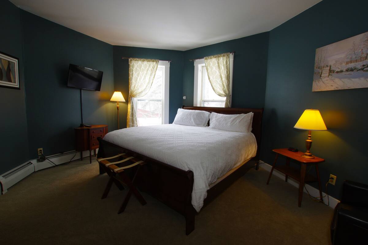 Une chambre à coucher avec un grand lit, deux lampes de chevet, un téléviseur fixé au mur et un tableau accroché au mur.