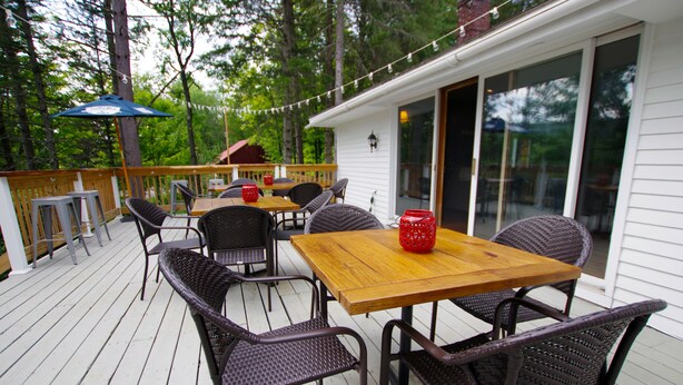 Eine Terrasse im Freien mit einem Holztisch und Korbstühlen, umgeben von einem Holzgeländer und Lichterketten.