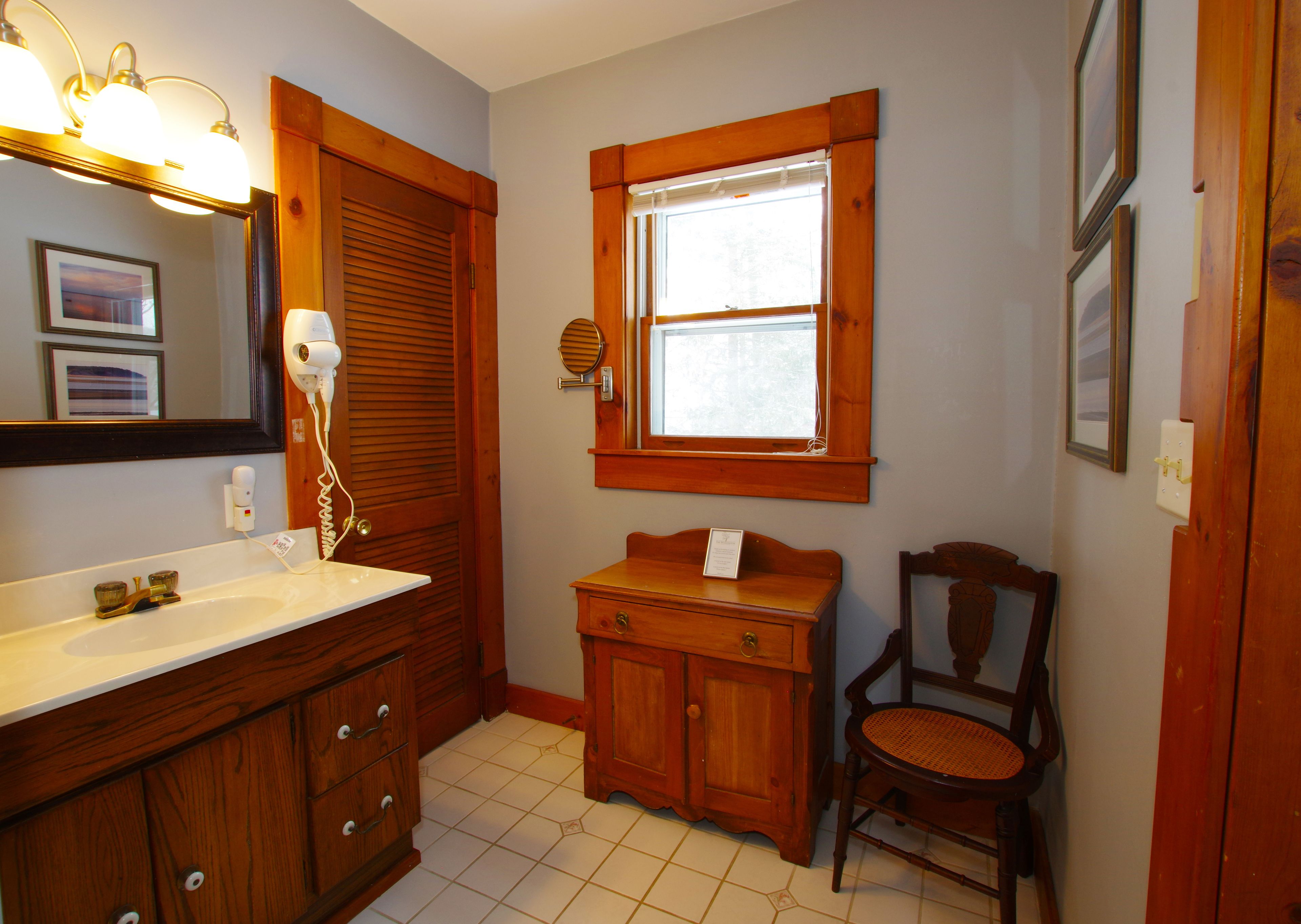 A bathroom with a wooden vanity, a chair, a mirror, and a window.
