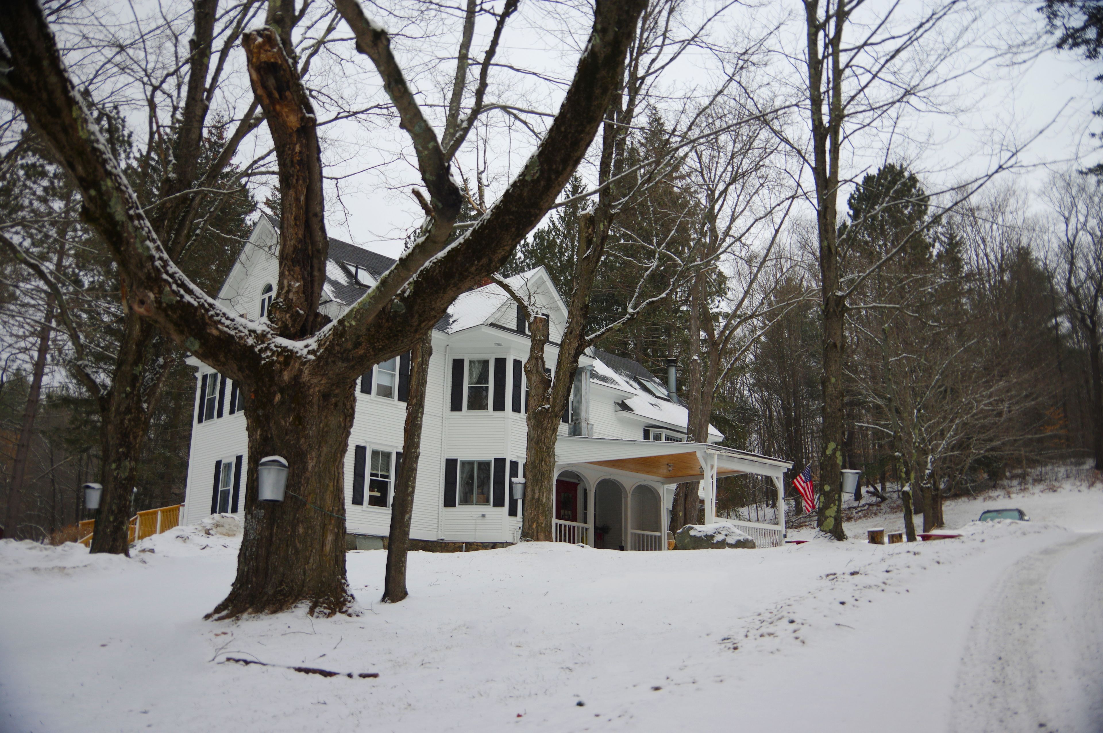 A two-story house with a porch and a garage, surrounded by snow-covered trees.
