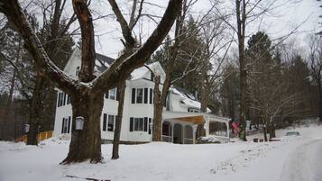 A two-story house with a porch and a garage, surrounded by snow-covered trees.
