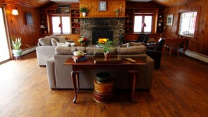 Ein gemütliches Wohnzimmer mit Kamin, Holzwänden, einer Couch und einem Essbereich.