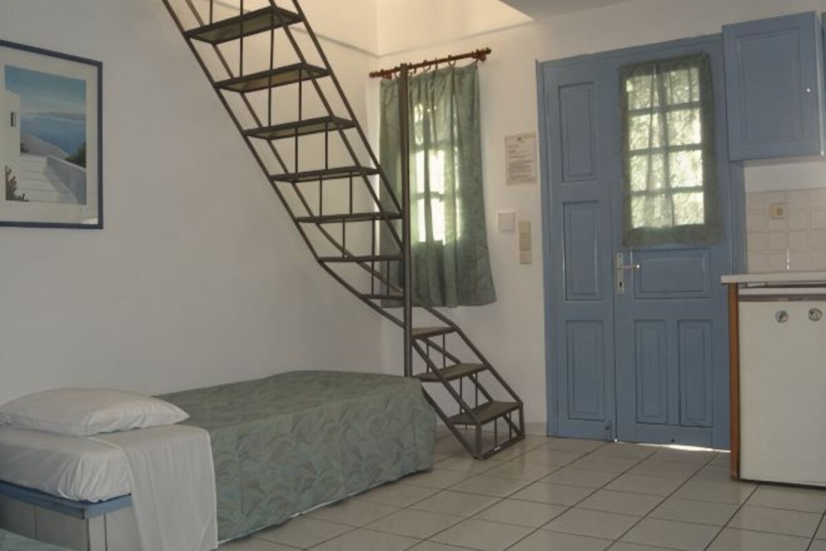 Un dormitorio con cama, una escalera, una puerta azul y una kitchenette.