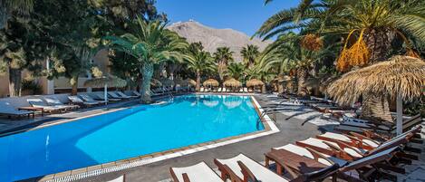 Una piscina al aire libre, sombrillas, sillones reclinables de piscina