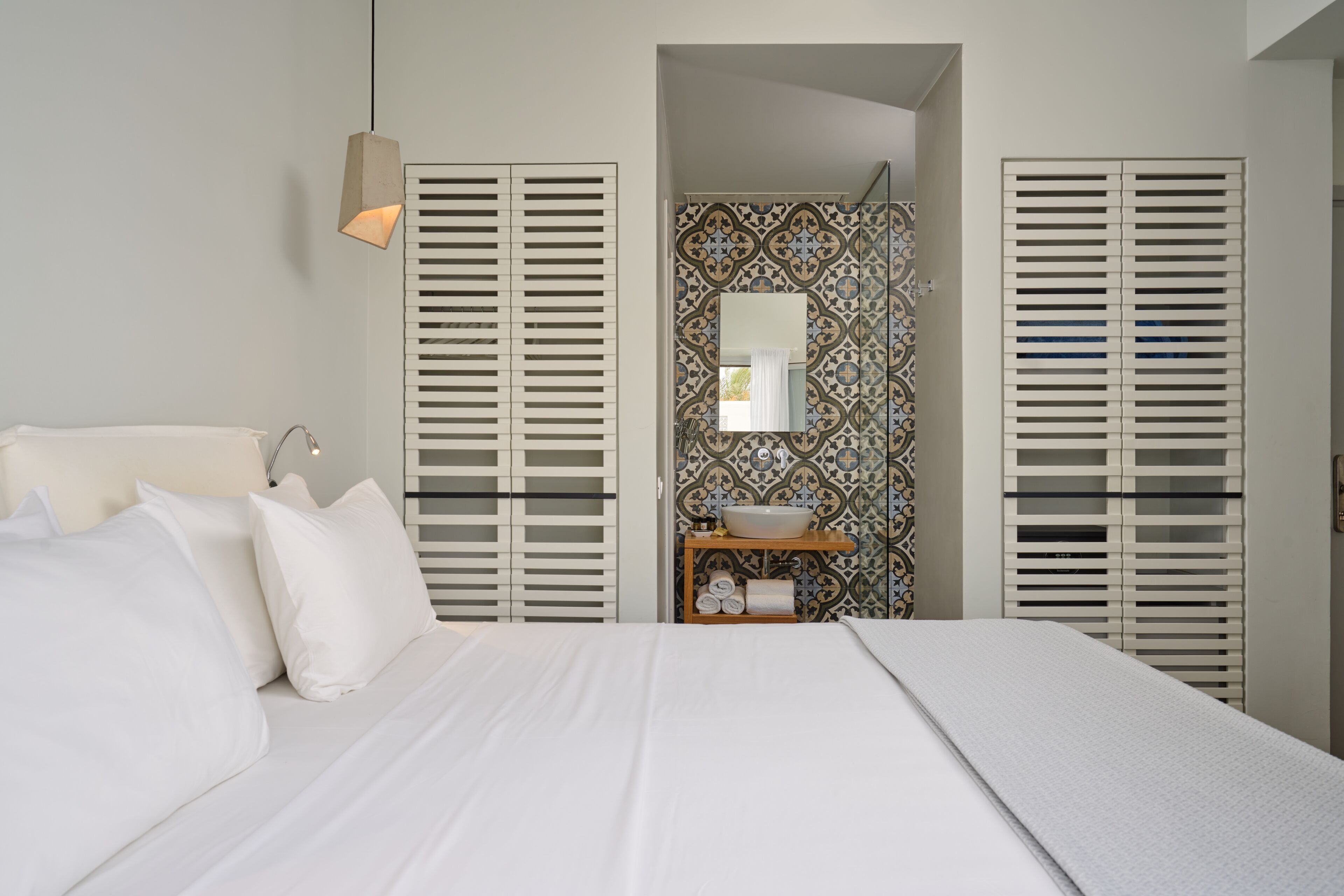 Een slaapkamer met een groot bed, een nachtkastje, een spiegel en een badkamer zichtbaar door een deur.