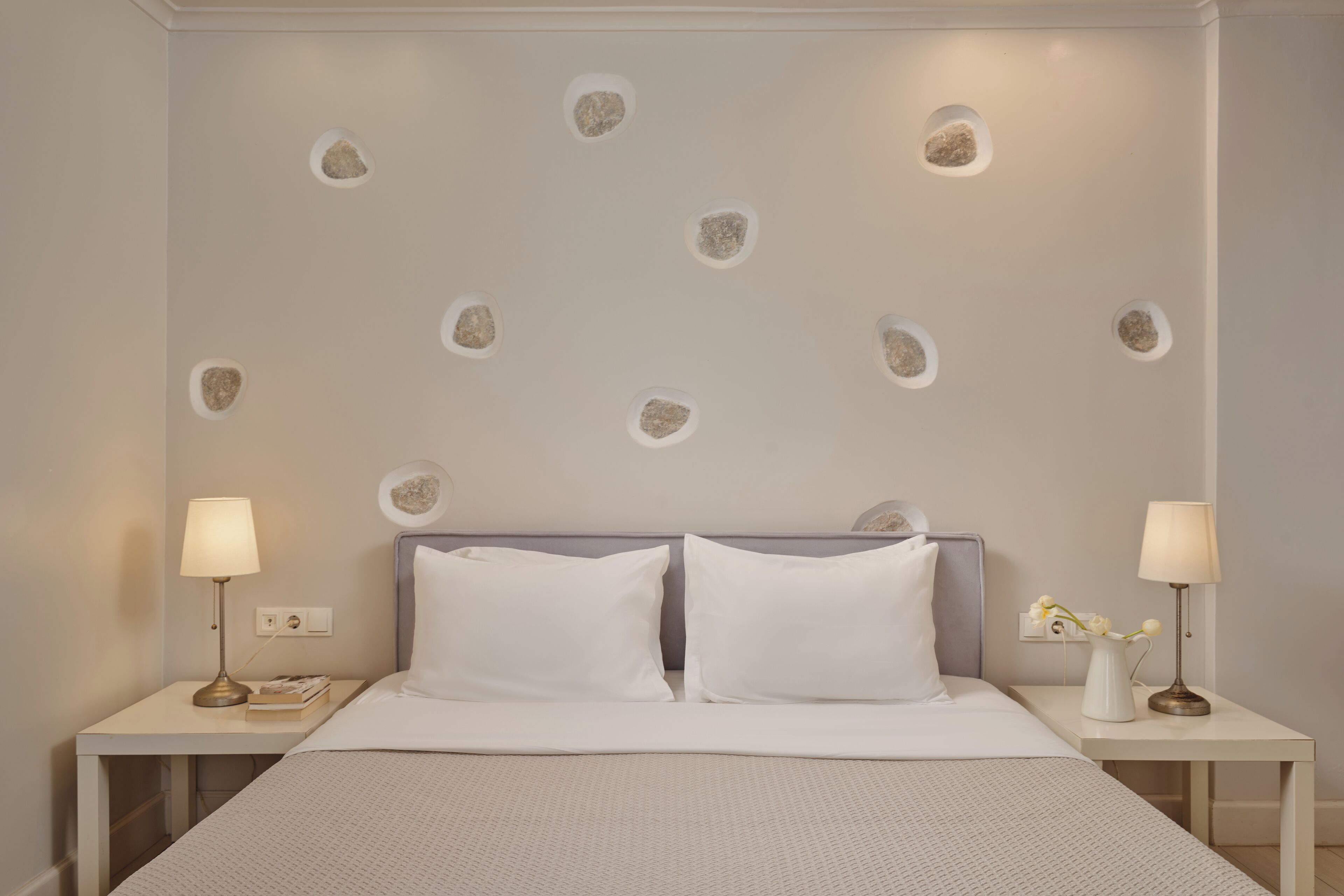 Habitación de hotel ordenada con una cama grande, dos mesitas de noche y una pared con elementos decorativos que imitan piedra.