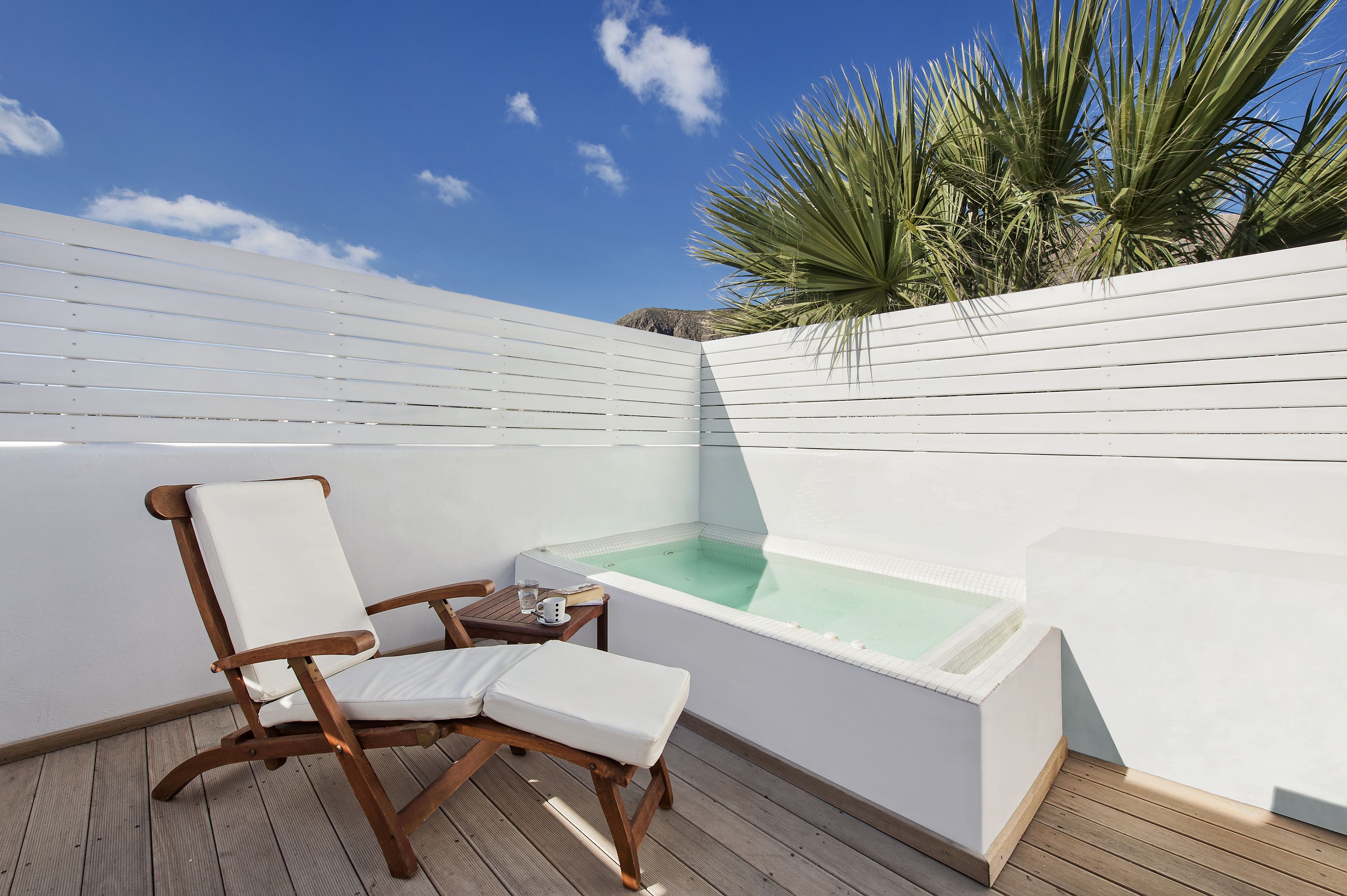 Una terraza de madera con una silla blanca acolchada, una mesita y un jacuzzi.