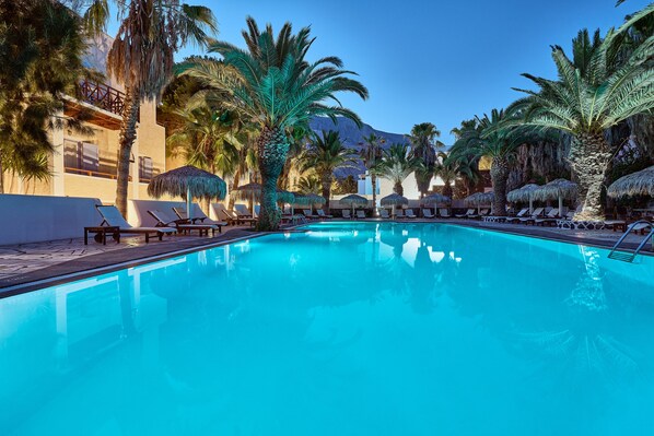 A swimming pool with lounge chairs and palm trees, surrounded by buildings with balconies.
