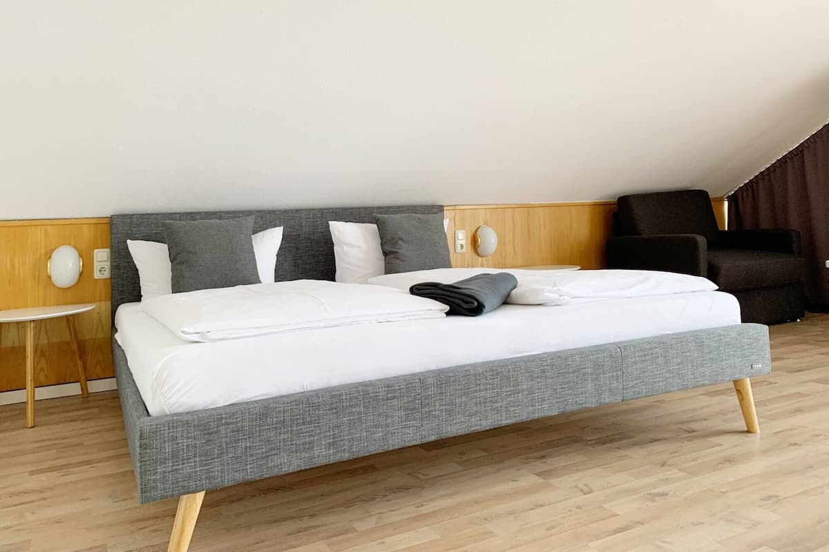 A modern hotel room with a large bed, a small round table, and a dark armchair.