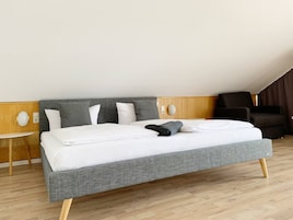 Una habitación de hotel moderna con una cama grande, una pequeña mesa redonda y un sillón oscuro.