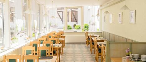 Un restaurante con sillas y mesas de madera, amplias ventanas y vistas a zonas verdes.