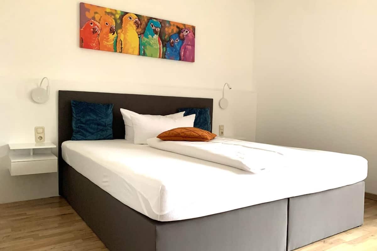 A modern bedroom with a large bed, a nightstand, and a painting above the bed.