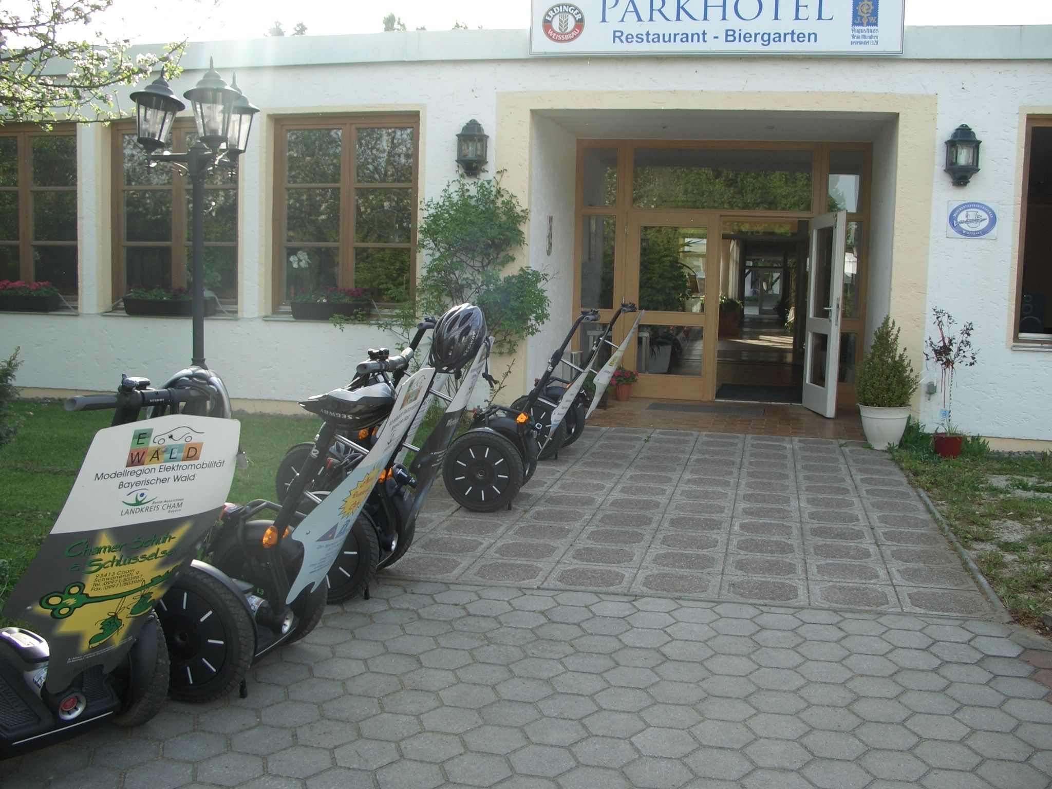 Entrada de un hotel con un camino pavimentado, un cartel y una fila de bicicletas estacionadas afuera.