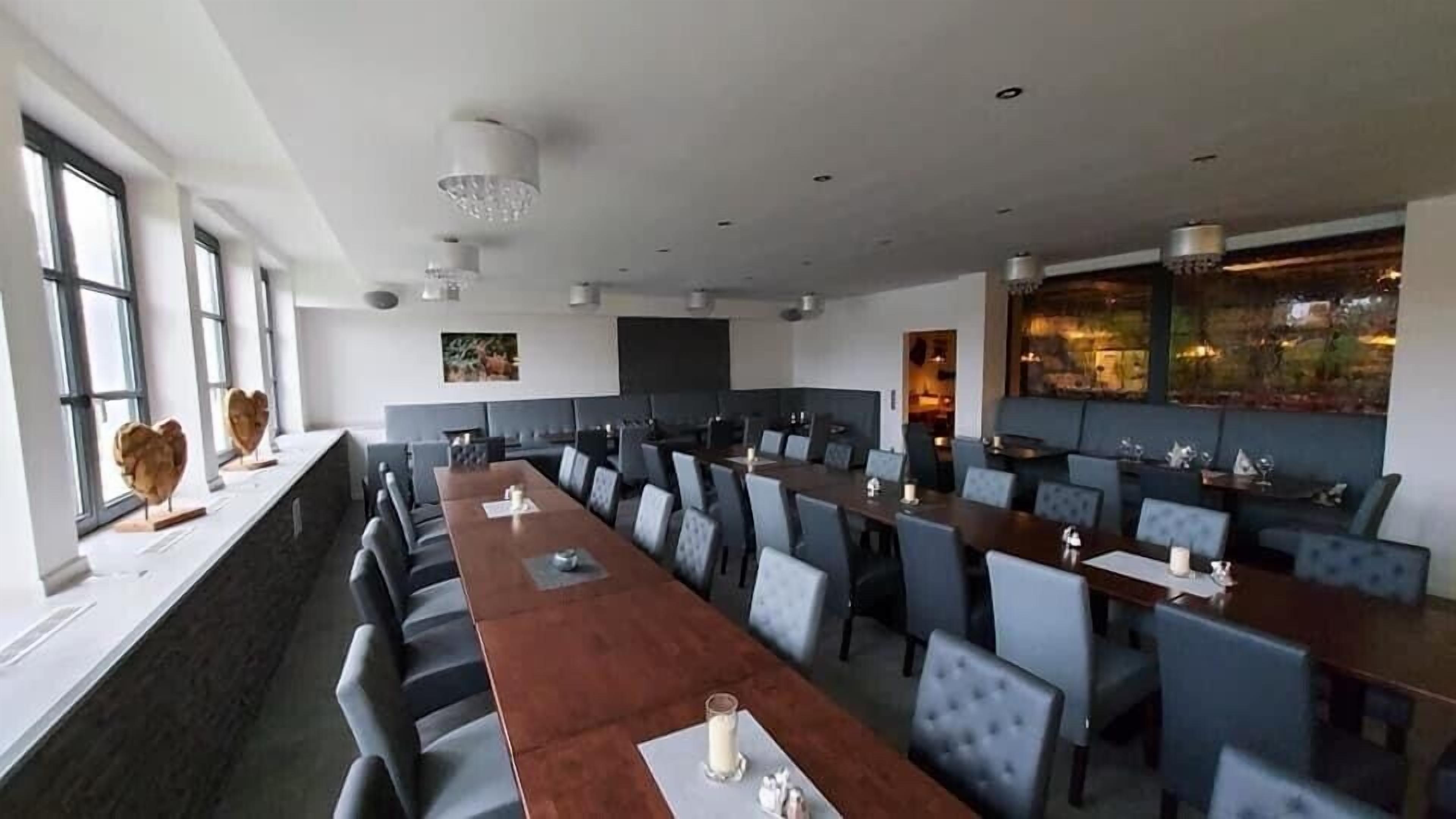 Un salón de conferencias con mesas y sillas largas, ventanas amplias y vistas al exterior.