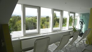 A room with large windows, white chairs, a radiator, and a view of greenery. - Parkhotel Cham (Cham)