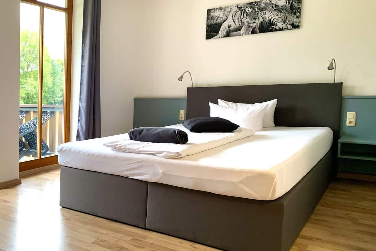 A modern hotel room with a large bed, a view of the outdoors, and a painting on the wall.