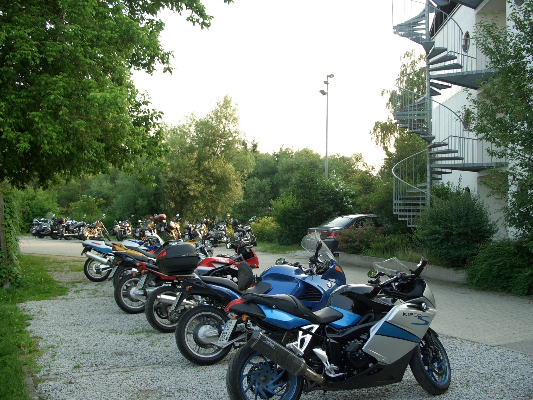 A row of parked motorcycles near a building with a spiral staircase.