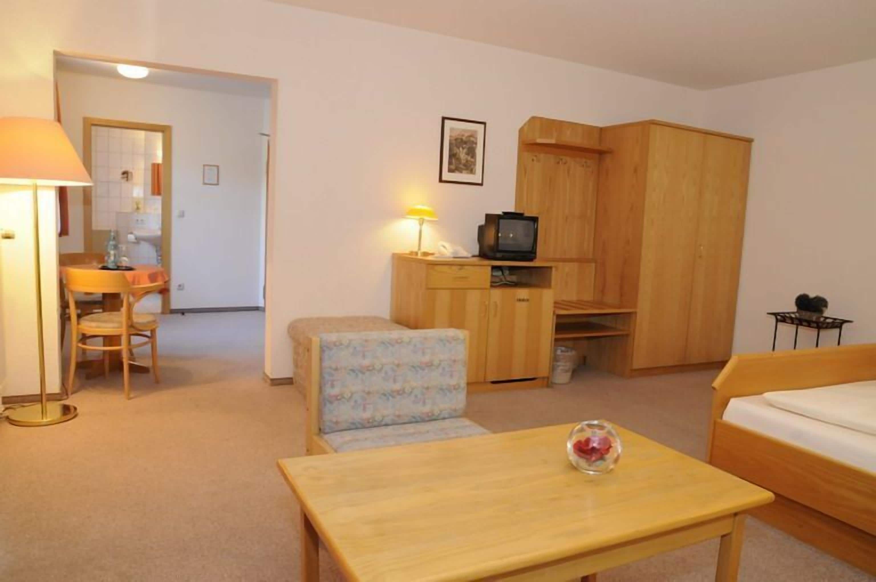 A compact room with a bed, a small desk with a lamp, a television, and a wardrobe.