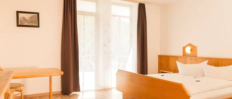 Una habitación de hotel con una cama y un escritorio de madera, una silla e imagen en la pared.