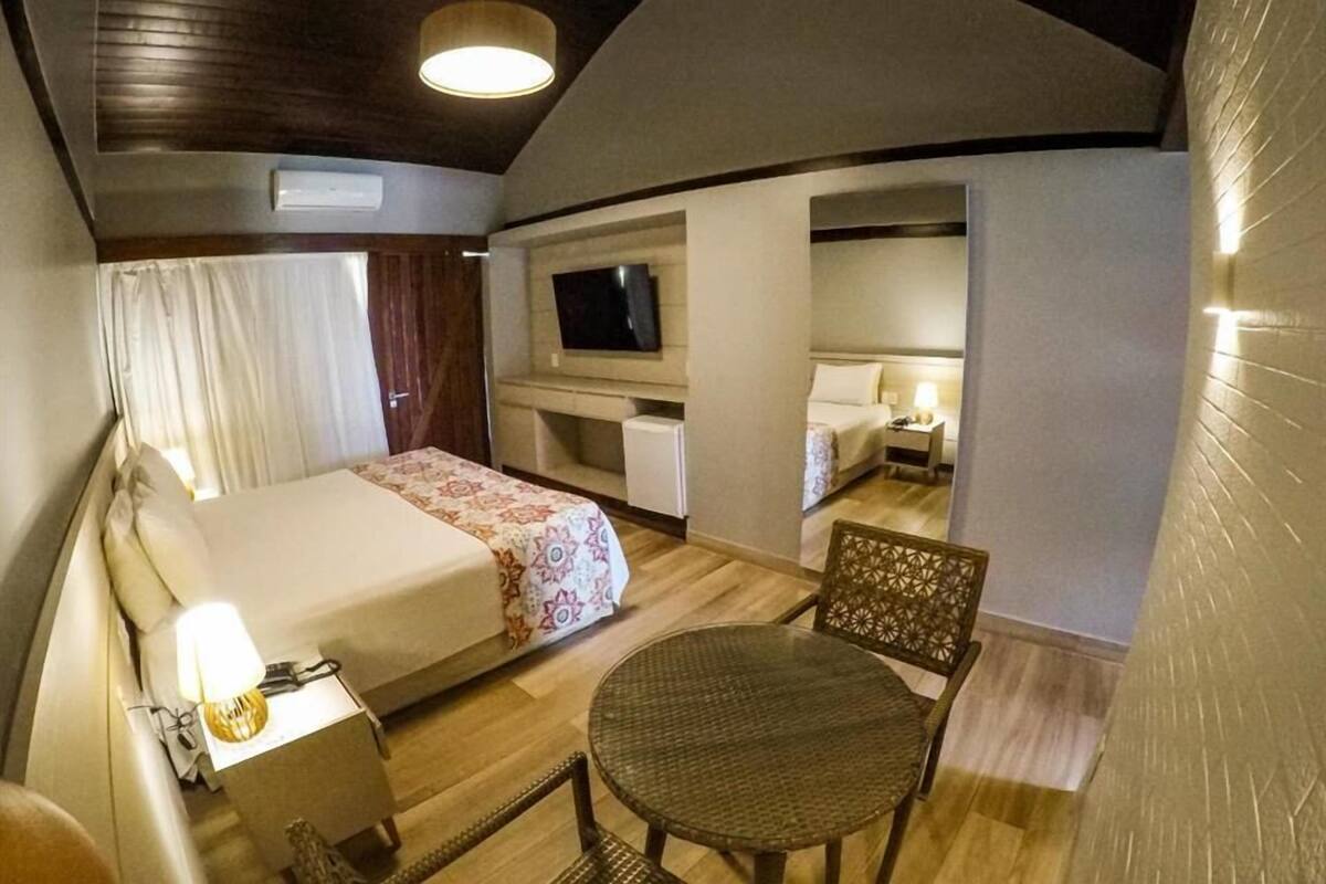 A cozy bedroom with a bed, bedside table, TV, and a small dining area.