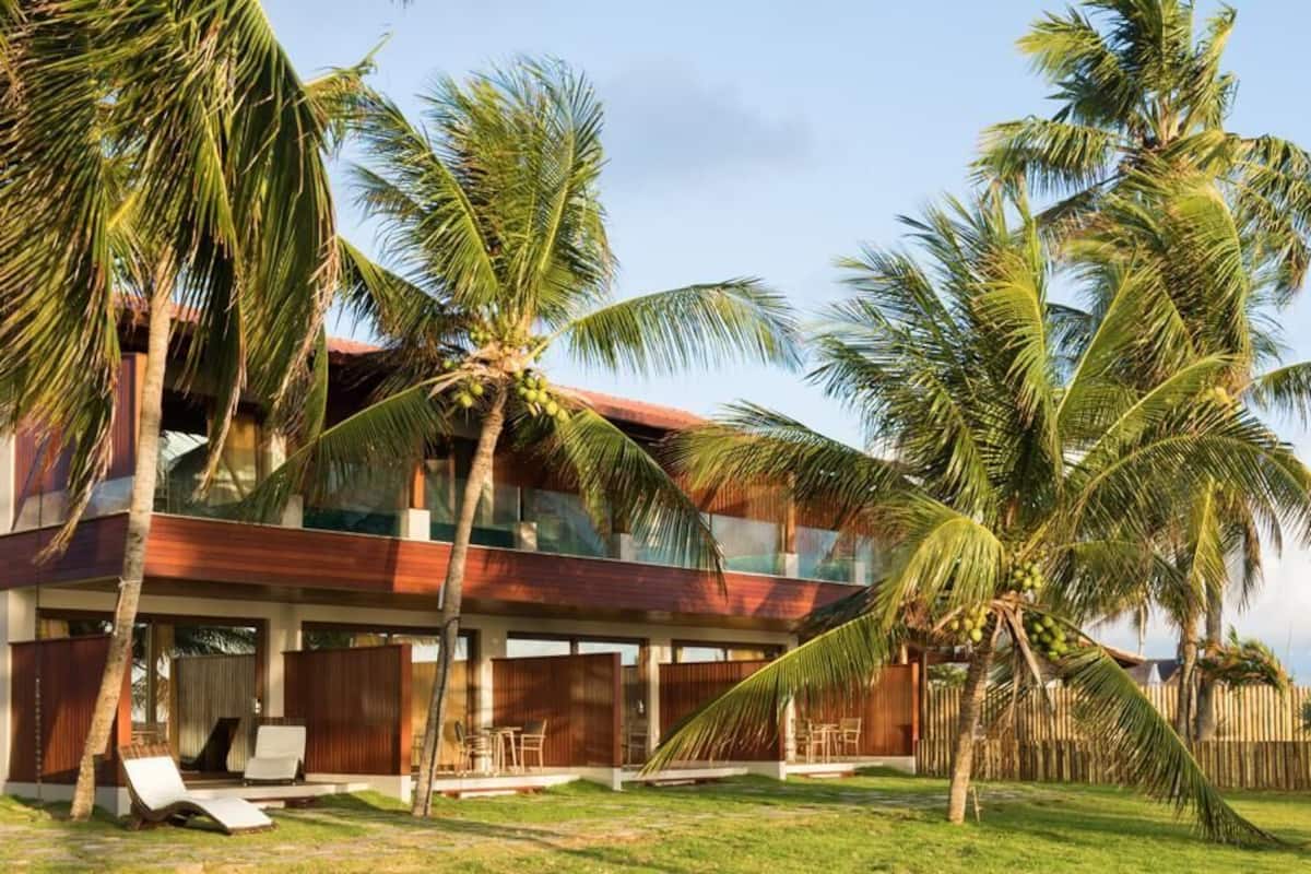 A modern house with a red roof, surrounded by palm trees and a wooden fence.