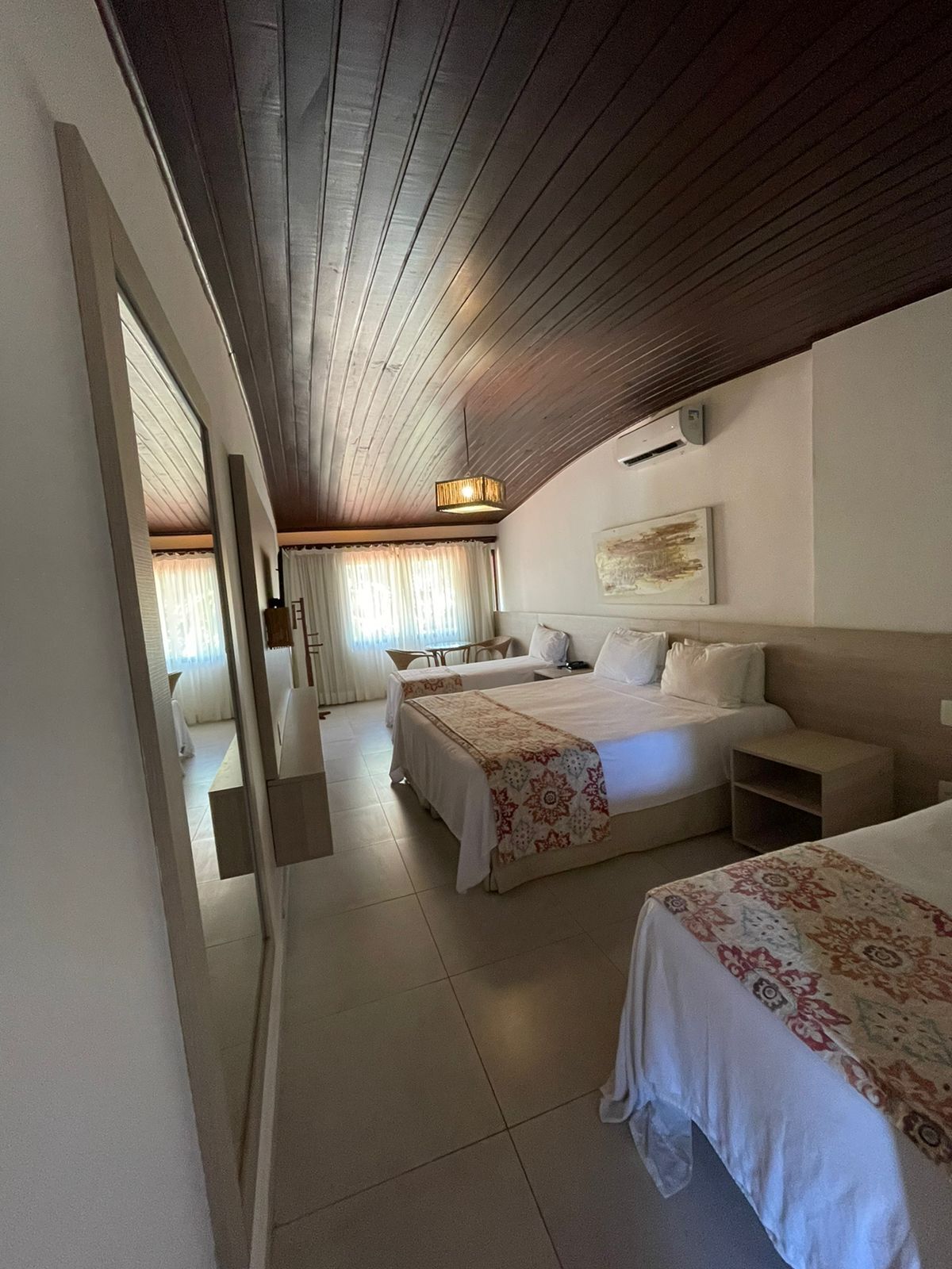 Habitación de hotel con dos camas, un espejo grande, un ventilador de techo y vista hacia otra habitación.