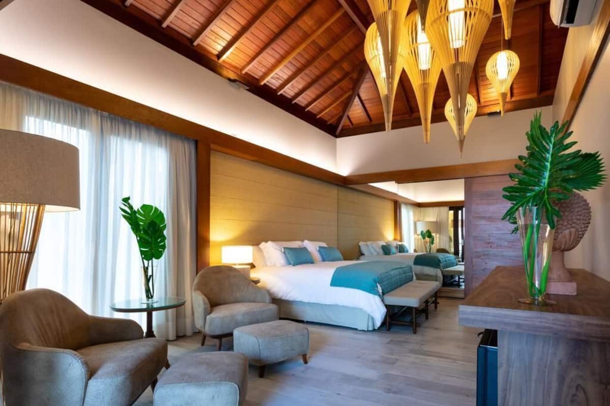 A modern hotel room with a large bed, two armchairs, a small table, and a wooden ceiling.